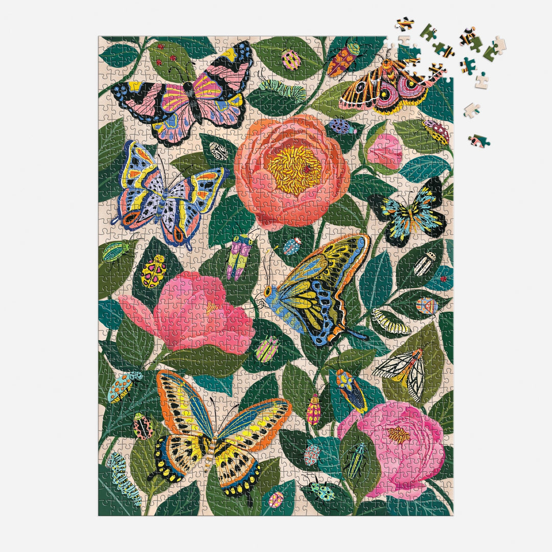 The Christine De Carvalho "Between the Blooms" 1000 Piece Foil Puzzle showcases vibrant butterflies and pink flowers with green leaves, with a few pieces missing in the top right corner.