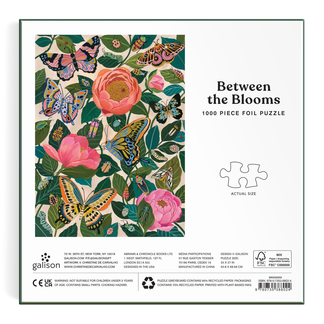 The image shows the back of the Christine De Carvalho "Between the Blooms 1000 Piece Foil Puzzle" box, featuring colorful butterflies and pink flowers among green leaves. The text reads Between the Blooms 1000 Piece Foil Puzzle.