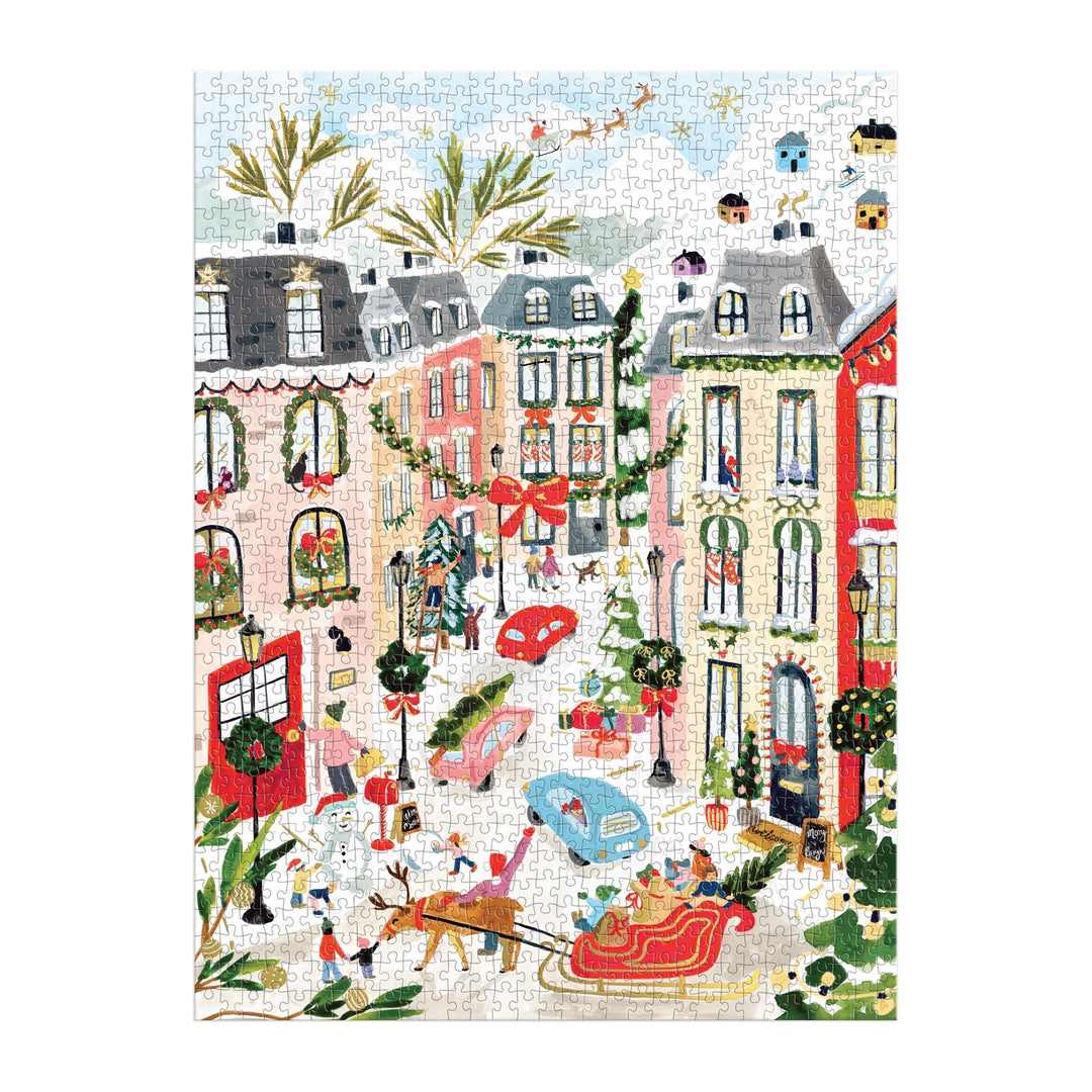 The Sabina Fenn Merriest Village 1000 Piece Foil Puzzle features an illustrated winter city scene with ice skaters, decorated buildings, snowy streets, and festive wreaths and garlands for a lively holiday vibe.