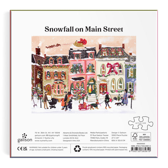Enjoy Nysha Lilly’s Snowfall on Main Street 1000 Piece Foil Puzzle, featuring a festive street scene with shoppers in the snow, colorful foil-accented buildings, a large wreath, and Santa’s sleigh above.