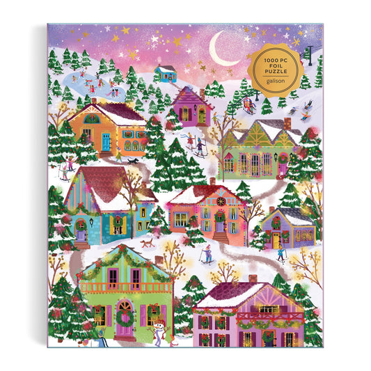 The Joy Laforme Snowcap Village 1000 Piece Foil Puzzle features a vibrant winter scene with snowy houses, trees, and skaters under a pink and purple evening sky, accented by shimmering foil details and a crescent moon.