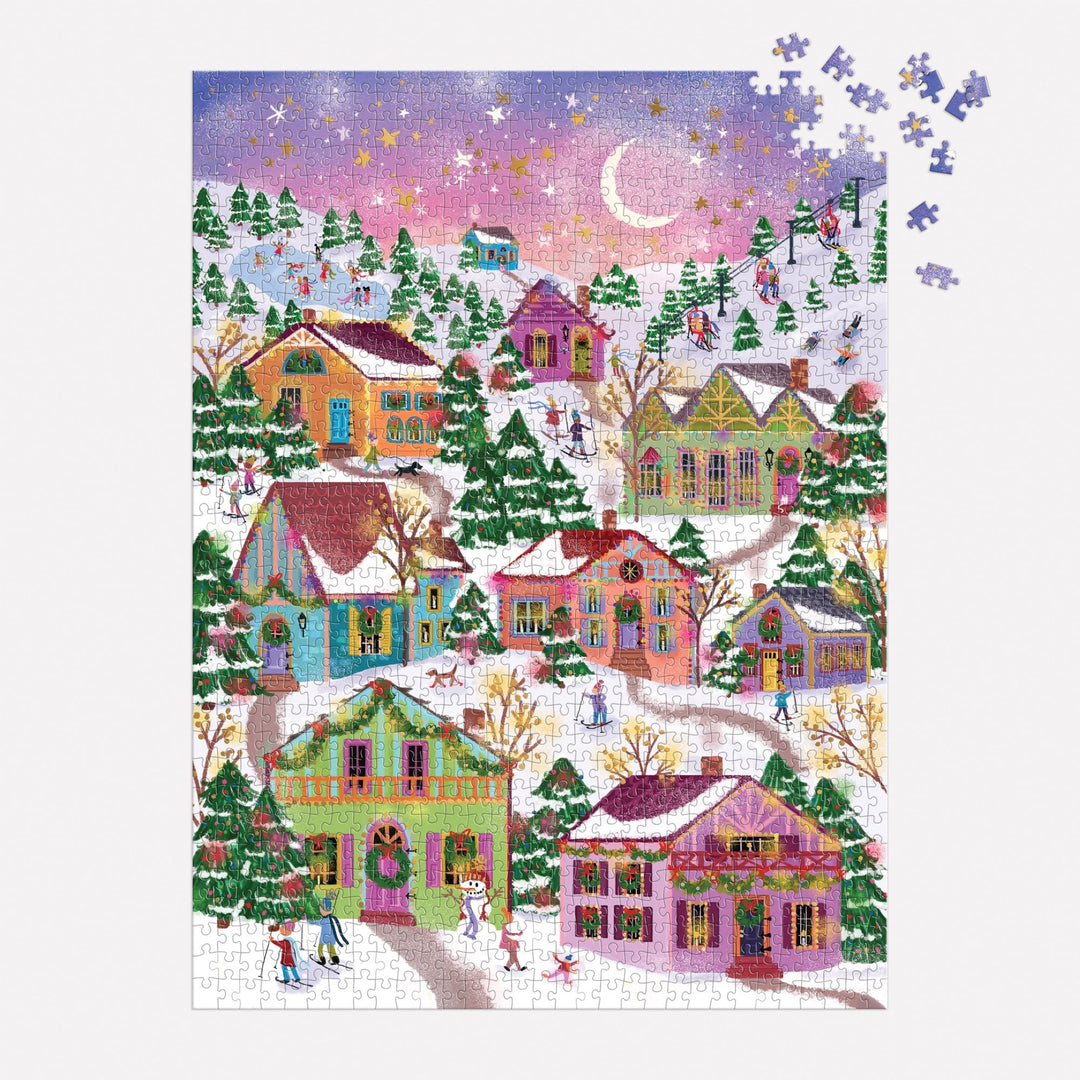 The Joy Laforme Snowcap Village 1000 Piece Foil Puzzle depicts a snowy village with pastel houses, pine trees, people strolling, and a pink-purple sky. A few pieces in the top right are missing from this charming Joy Laforme scene.