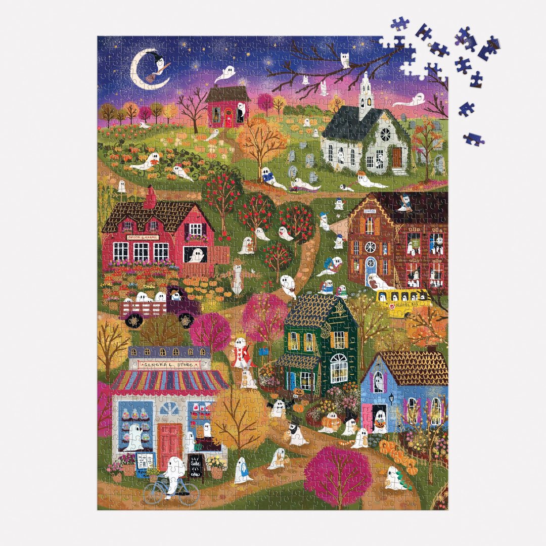 The Joy Laforme Spooky Village 1000 Piece Foil Puzzle features a whimsical night scene with ghosts, houses, gravestones, and a crescent moon under sparkling foil accents. Several loose pieces are placed in the top right corner.