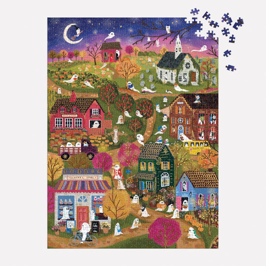 The Joy Laforme Spooky Village 1000 Piece Foil Puzzle features a whimsical night scene with ghosts, houses, gravestones, and a crescent moon under sparkling foil accents. Several loose pieces are placed in the top right corner.