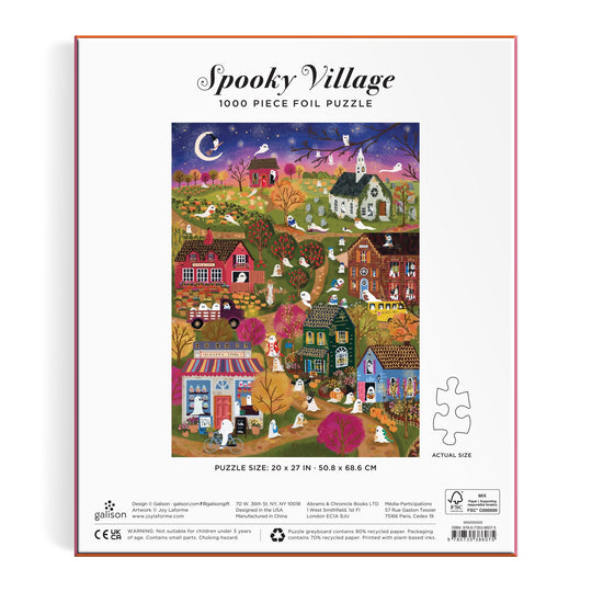Box for the Joy Laforme Spooky Village 1000 Piece Foil Puzzle, featuring vibrant Halloween houses, ghosts, pumpkins, and a moonlit sky. The completed puzzle image appears on the box. Brand: Joy Laforme.