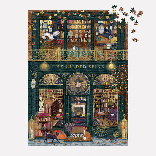 The Gilded Spine 1000 Piece Foil Puzzle by Sally Wilson features a cozy bookstore with cats, books, glowing lamps, and missing pieces in the top right corner. A dog and fox sit at the entrance, adding to the charming scene.