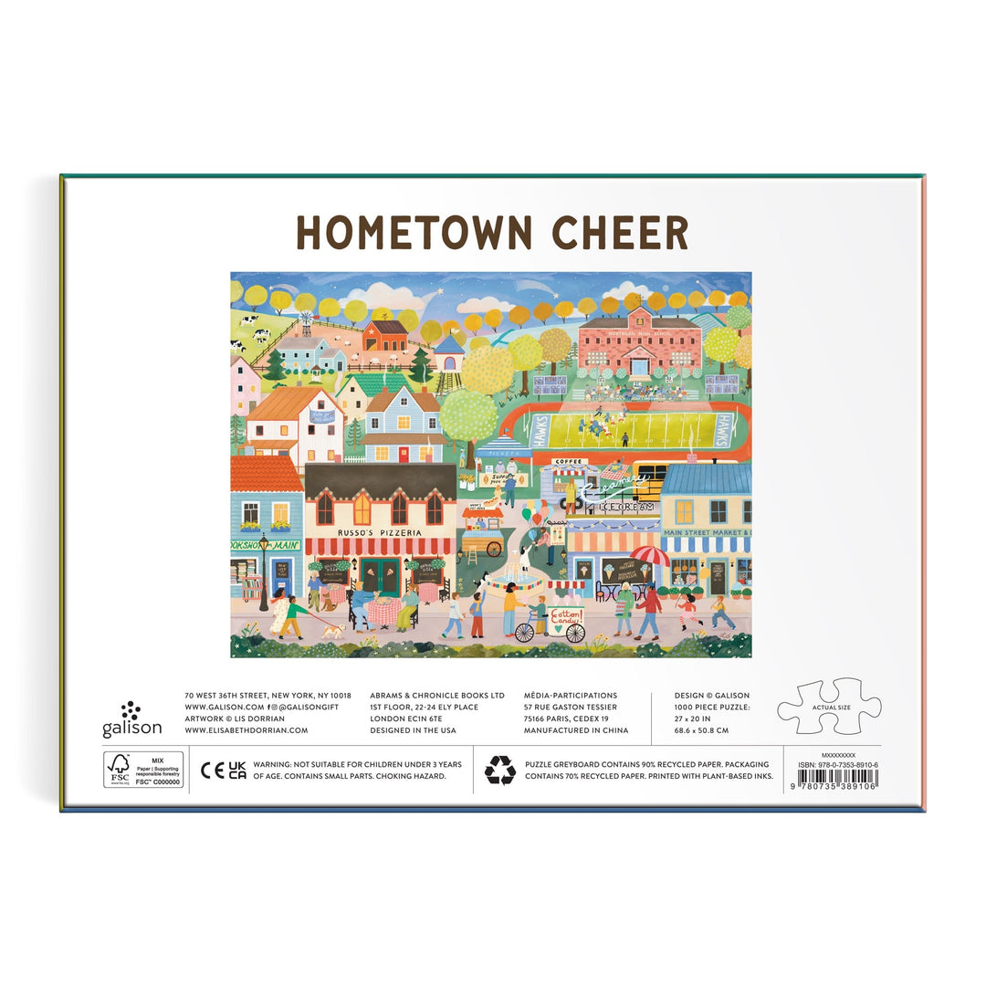Box back for the Elisabeth Dorrian Hometown Cheer 1000 Piece Puzzle, featuring a vibrant small-town scene with people, houses, shops, trees, blue sky, clouds, and balloons.