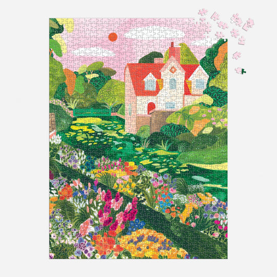 The Blooming Meadow 1000 Piece Puzzle by Flore Cousseran features a vibrant garden of flowers, lush greenery, and a white house with a red roof, with just a few pieces left to complete in the upper right corner.