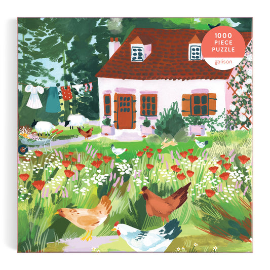 Joanna Clay’s Cottage Wildflowers 1000 Piece Puzzle in a Square Box features a red-roofed cottage, wildflowers, chickens, and laundry on a line—a charming countryside scene for puzzlers to enjoy.