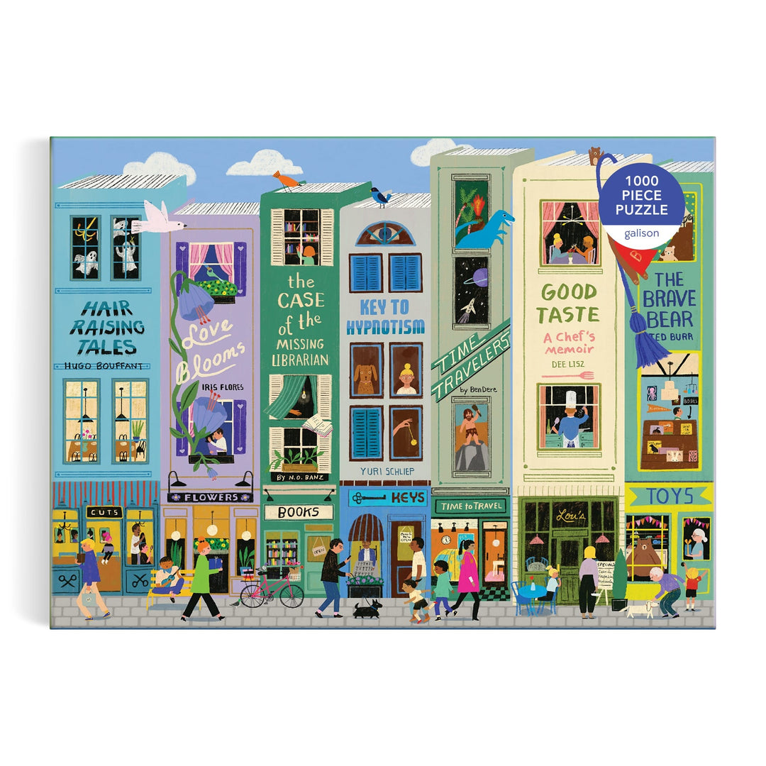 The Anne Bentley Main Street Books 1000 Piece Puzzle features a colorful illustrated box with whimsical book-themed storefronts, lively street scenes, and people walking by vibrant shop windows.