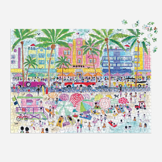 The Michael Storrings South Beach Miami 1000 Piece Puzzle by Michael Storrings features a vibrant beach scene with people, umbrellas, palm trees, and art deco buildings. A few pieces are missing in the top right corner.