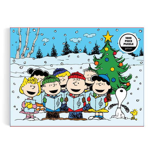 Cartoon children and Snoopy sing carols by a decorated tree in the snow, holding songbooks as a yellow bird stands nearby. The Peanuts Christmas Caroling 1000 Piece Puzzle by Peanuts Worldwide, LLC label is visible.