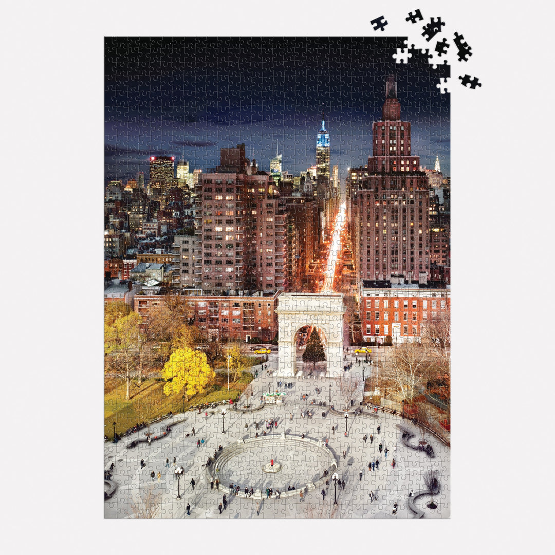 The Stephen Wilkes Day To Night Washington Square Park 1000 Piece Puzzle by Stephen Wilkes shows a vibrant NYC nighttime cityscape with the illuminated arch and skyline; a few pieces are missing in the top right corner.