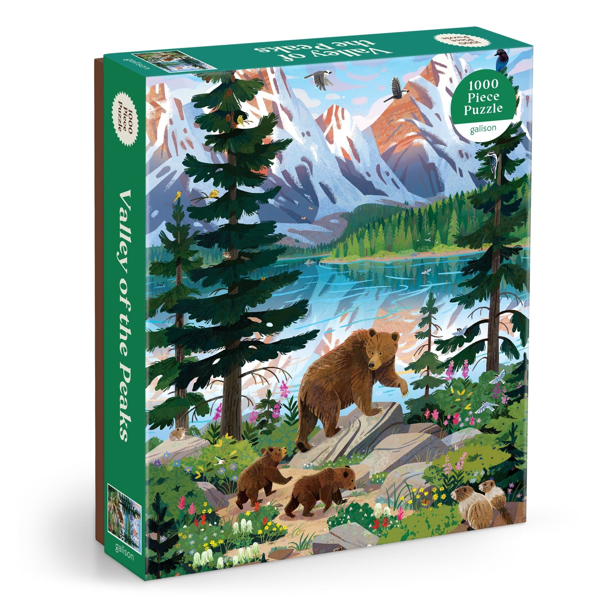 The Kim Smith Valley of the Peaks 1000 Piece Puzzle features a bear with cubs walking by a mountain lake, with snow-capped peaks and wildlife in the background.
