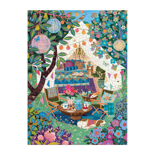 The Victoria Ball Blooming Escape 1000 Piece Puzzle by Victoria Ball features a cozy outdoor tea party with a tent, colorful rugs, chairs, a tea table with pastries, lanterns, bunting, flowers, lush greenery, and a dog resting on the grass.
