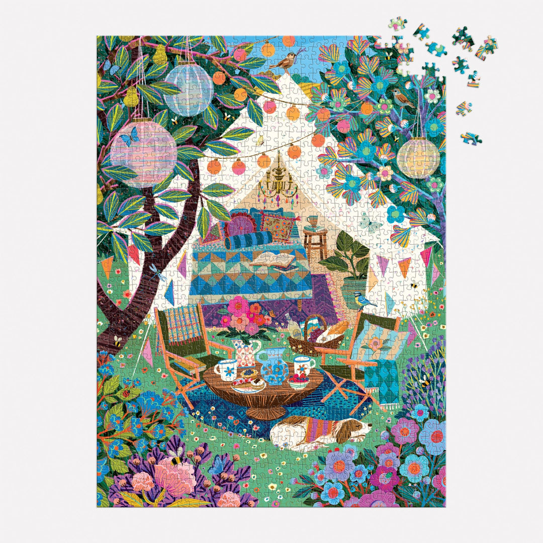 The Victoria Ball Blooming Escape 1000 Piece Puzzle by Victoria Ball features a colorful outdoor picnic scene with a tent, lanterns, armchairs, treats, and vibrant flowers. A few pieces remain unplaced in the top right corner.