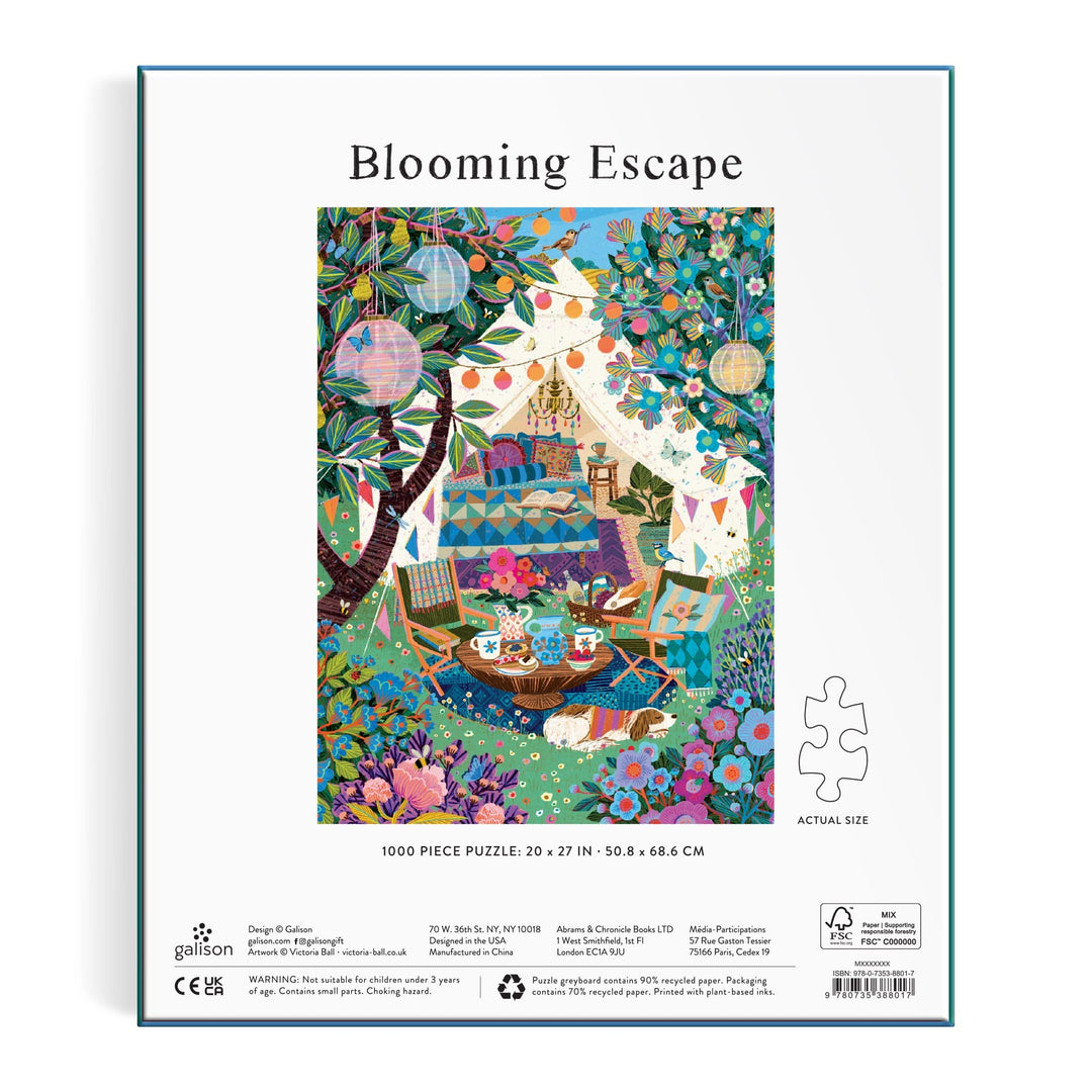The image features a vibrant outdoor camping scene with a tent, picnic, blankets, flowers, trees, lanterns, and bunting. It appears on the box of the Victoria Ball Blooming Escape 1000 Piece Puzzle by Victoria Ball.
