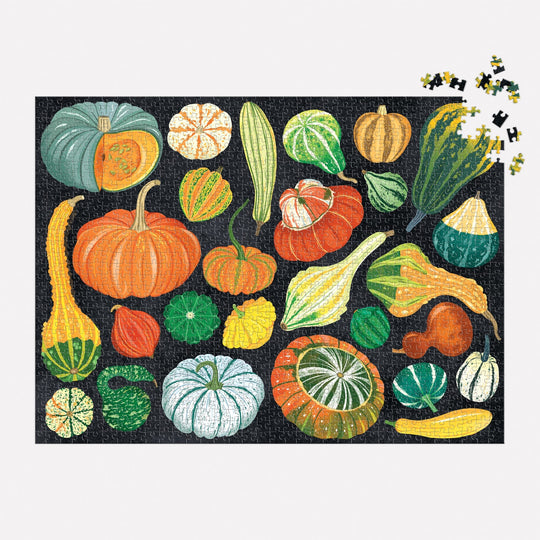 The World of Pumpkins 1000 Piece Puzzle by Dawn Cooper features vibrant illustrations of pumpkins and gourds on a black background, with several loose pieces visible in the top right corner.