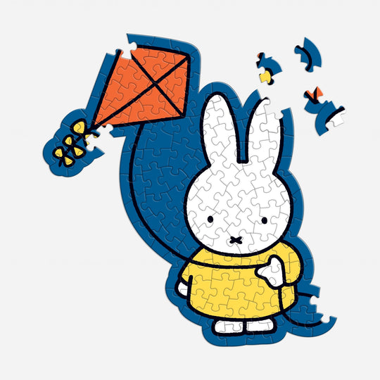 The Miffy 100 Piece Surprise Puzzle by Miffy features a partially completed image of the white bunny in a yellow dress holding an orange kite, with several pieces missing from the top right corner.