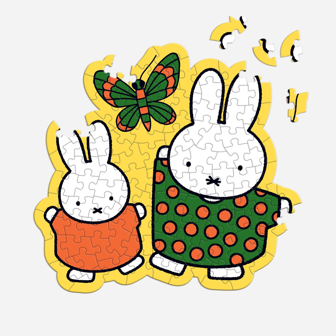 In the Miffy 100 Piece Surprise Puzzle by Miffy, two cartoon rabbits—one in orange, one in green with red dots—stand together as a butterfly flies above. Four puzzle pieces are missing from the top right corner.