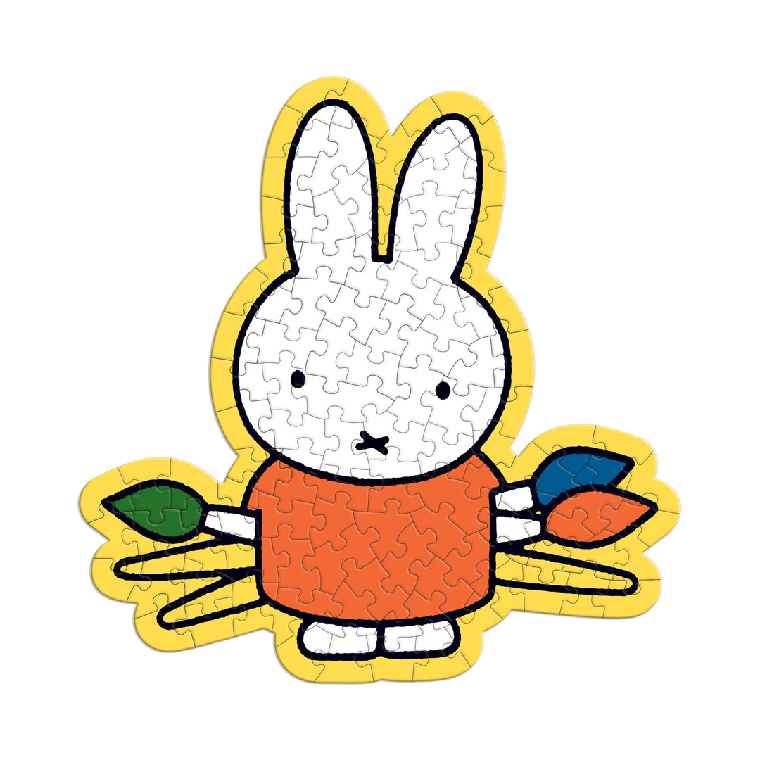 The Miffy 100 Piece Surprise Puzzle by Miffy features a cartoon white bunny with long ears, wearing an orange shirt and holding green, orange, and blue leaves, all outlined with a thick yellow border.