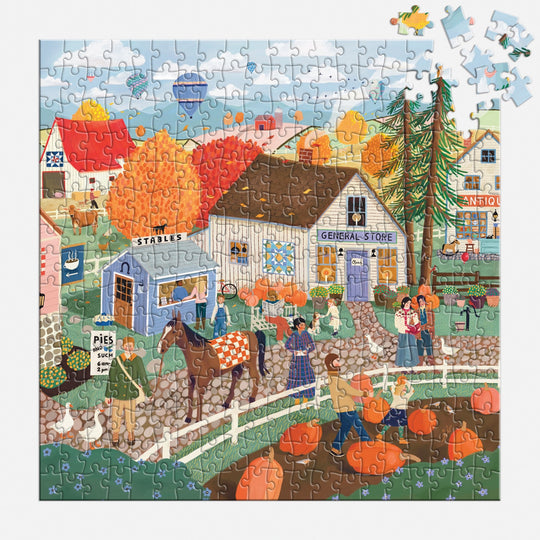 The Autumn Square 300 Piece Puzzle by Elisabeth Dorrian features a vibrant fall village with people, pumpkins, animals, and charming shops among autumn trees. A few pieces are missing in the top right section of this lively scene.