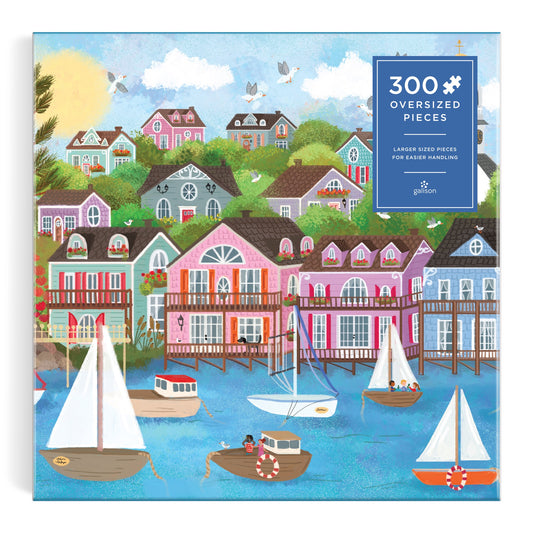 The Joy Laforme Harbor by the Sea 300 Piece Puzzle features colorful coastal houses, boats on blue water, and a bright sky. Oversized pieces make this Joy Laforme puzzle easy to handle.