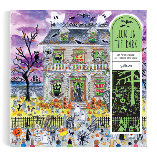 The Michael Storrings Haunted House 500 Piece Glow in the Dark Puzzle features a Halloween scene with ghosts, pumpkins, bats, skeletons, and costumed trick-or-treaters under a purple sky—perfect for intermediate puzzlers.