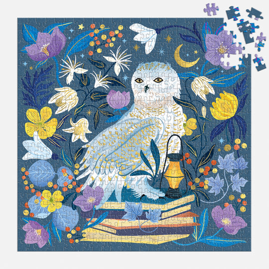 A nearly finished Dawn Cooper Celestial Owl 500 Piece Foil Puzzle displays a white owl on books, surrounded by vibrant flowers and stars on a dark blue background, with some pieces missing from the top right corner.