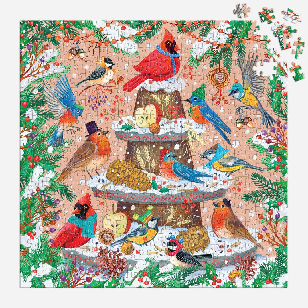 The Festive Feathers 500 Piece Foil Puzzle by Olga Akbarova features cardinals, robins, and blue jays amid snowy pinecones, holly, berries, and leaves. Some pieces in the top right corner remain unfinished for added fun.