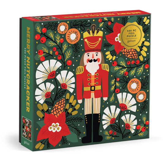 The Merry Nutcracker 500 Piece Foil Puzzle by Sandra Hutter features festive art with a red-uniformed nutcracker among white flowers, red berries, and green foliage for a vibrant holiday collectible.