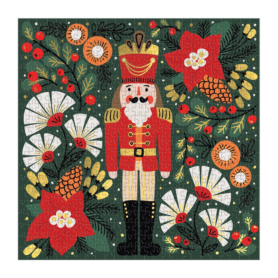 The Merry Nutcracker 500 Piece Foil Puzzle by Sandra Hutter features a nutcracker in a red uniform surrounded by festive flowers, pinecones, berries, foliage, and snowflakes—an ideal holiday-themed collector’s puzzle.