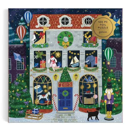 The Bex Parkin Twilight Toy Shop 500 Piece Foil Puzzle features a festive toy shop with wreaths, lights, candy canes, toys in the windows, hot air balloons above, a nutcracker and black cat outside—all beneath falling snow.