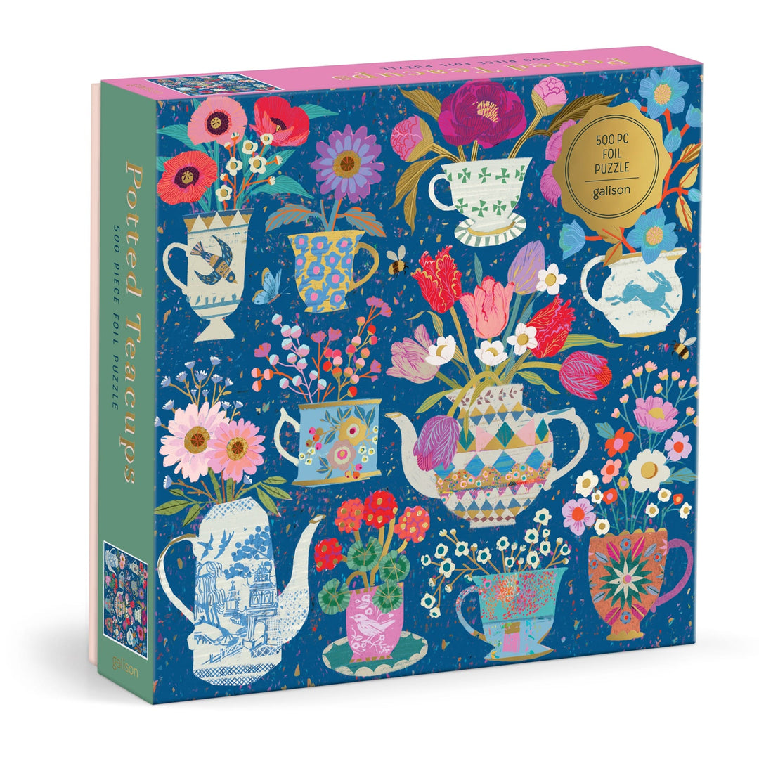 The Victoria Ball Potted Teacups 500 Piece Foil Puzzle features vibrant teacup and teapot illustrations with flowers on a blue backdrop, gold foil accents, and "Potted Teacups" written along the side of the box.