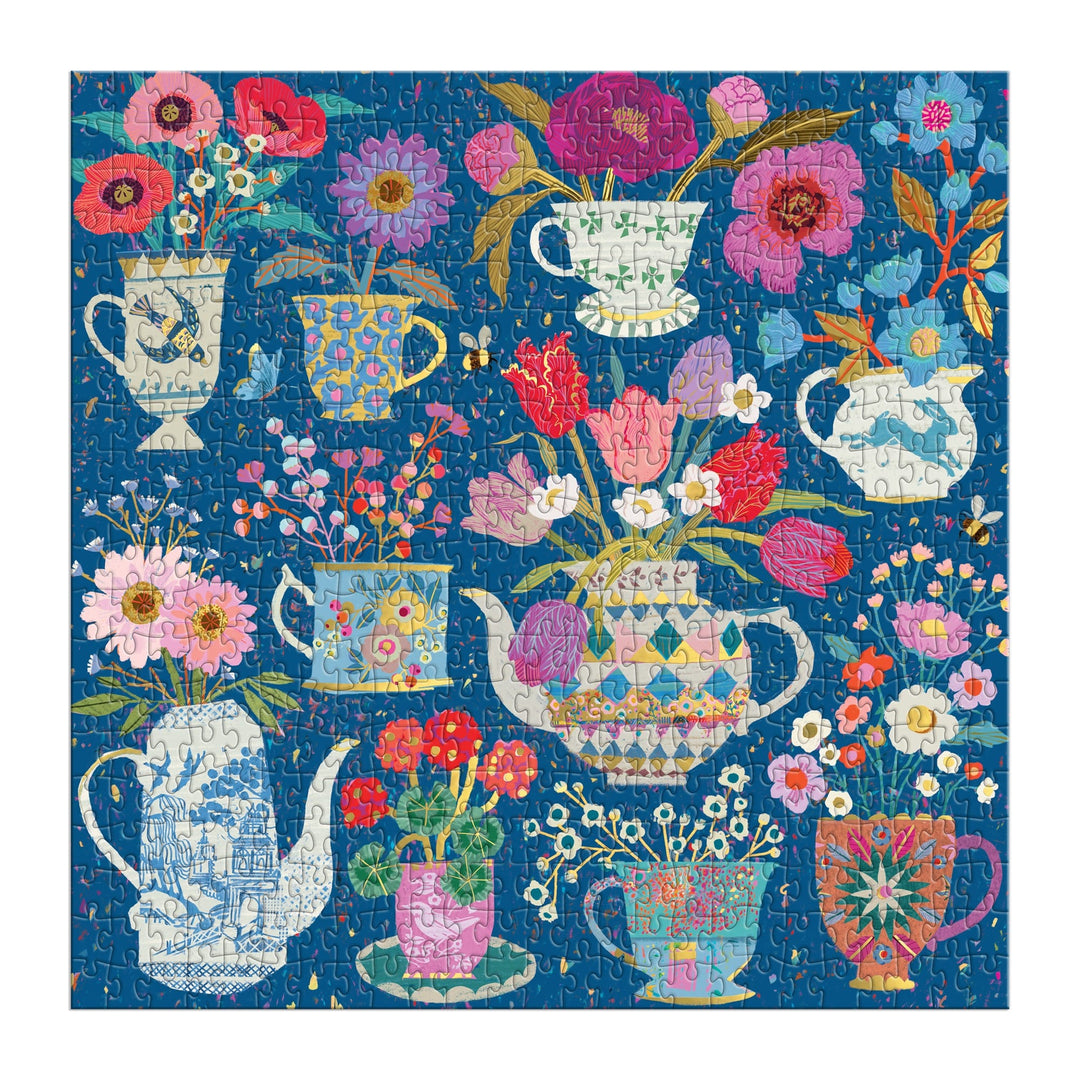The Victoria Ball Potted Teacups 500 Piece Foil Puzzle by Victoria Ball features vibrant flowers in teapots, mugs, and pitchers on a blue background, all illustrated in colorful patterns and shades of pink, red, purple, and blue.