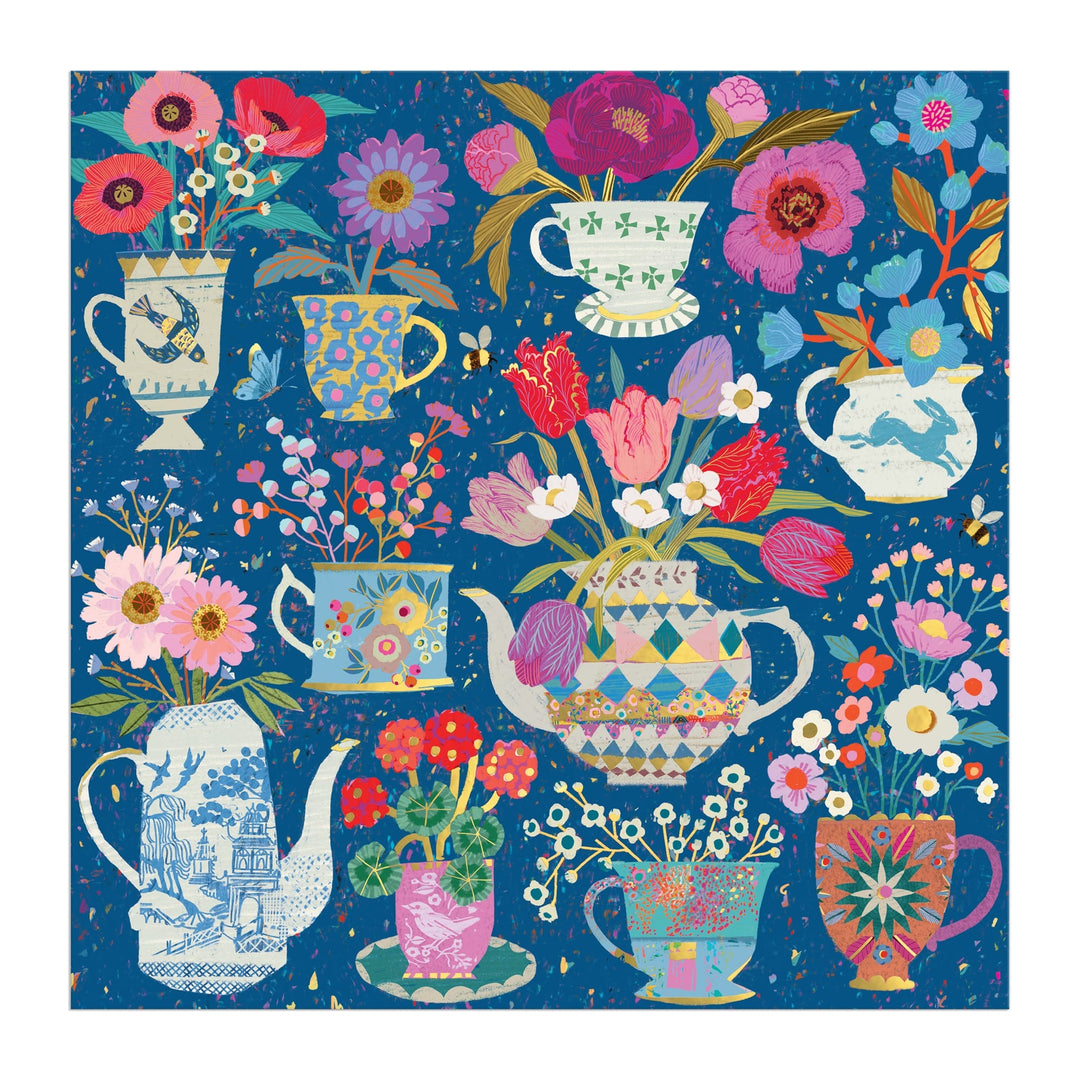 The Victoria Ball Potted Teacups 500 Piece Foil Puzzle features colorful teapots and teacups brimming with bright flowers, set on a blue textured background with vibrant floral and geometric patterns. Brand: Victoria Ball.