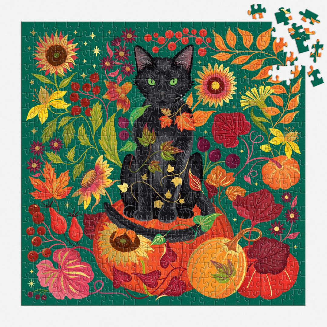 The Whiskers of Autumn 500 Piece Foil Puzzle by Dawn Cooper features a black cat on pumpkins amid autumn leaves, sunflowers, and berries against a green backdrop, with some pieces missing in the top right corner.