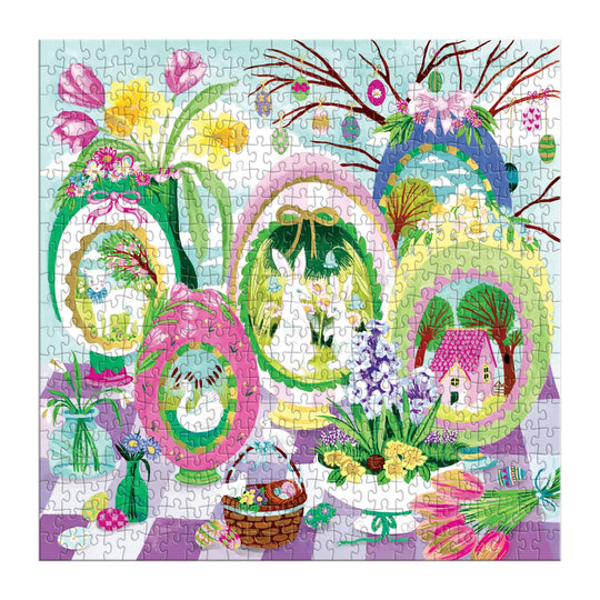 The Windows to Spring 500 Foil Piece Puzzle by Joanna Clay features painted egg-shaped frames with spring scenes—rabbits, flowers, a house—and details like vases, a basket, and pastel décor on a checkered table.