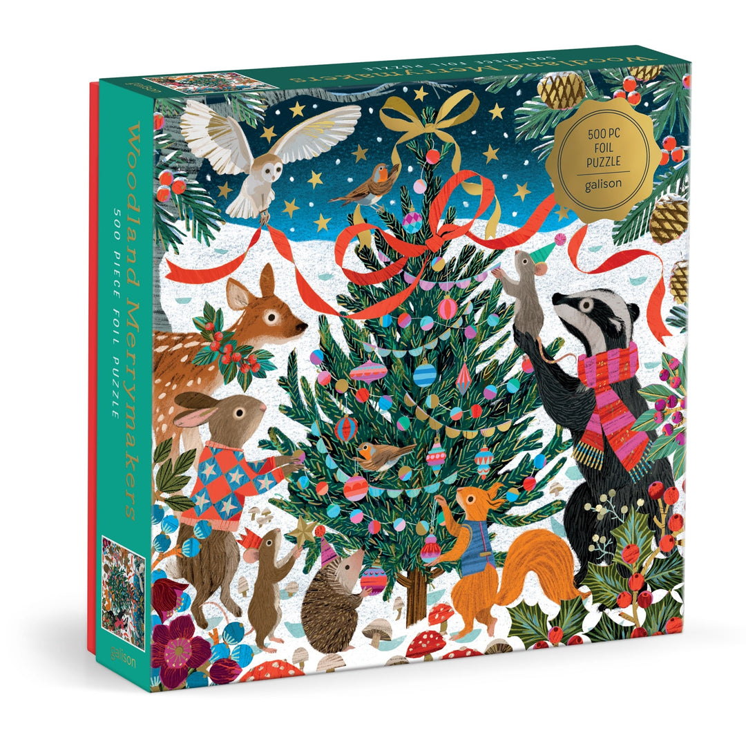 The Victoria Ball Woodland Merrymakers 500 Piece Foil Puzzle by Victoria Ball features woodland animals like a badger, fox, deer, and owl decorating a Christmas tree in a snowy, festive scene with bright colors and pine branches.