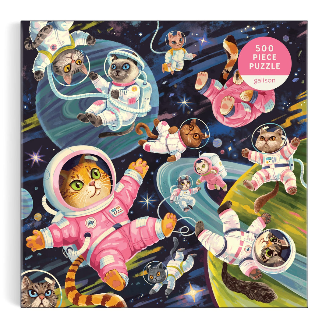 A Space Meowdyssey 500 Piece Puzzle by Lucia Baertl features colorful cats in spacesuits floating among stars, vibrant planets, and swirling patterns in a whimsical outer space scene.