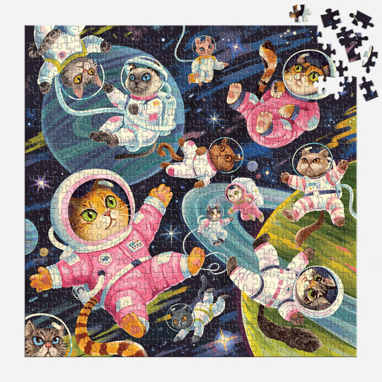 The Lucia Baertl "A Space Meowdyssey 500 Piece Puzzle" showcases cartoon cats in astronaut suits floating among planets and stars. The nearly finished puzzle has a few missing pieces in the top right corner.