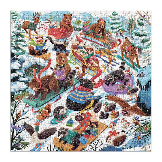 The Dashing All the Way 500 Piece Puzzle by Lucia Baertl features animals like bears, raccoons, otters, and birds sledding and playing in a snowy forest winter scene with trees and snow-covered hills.