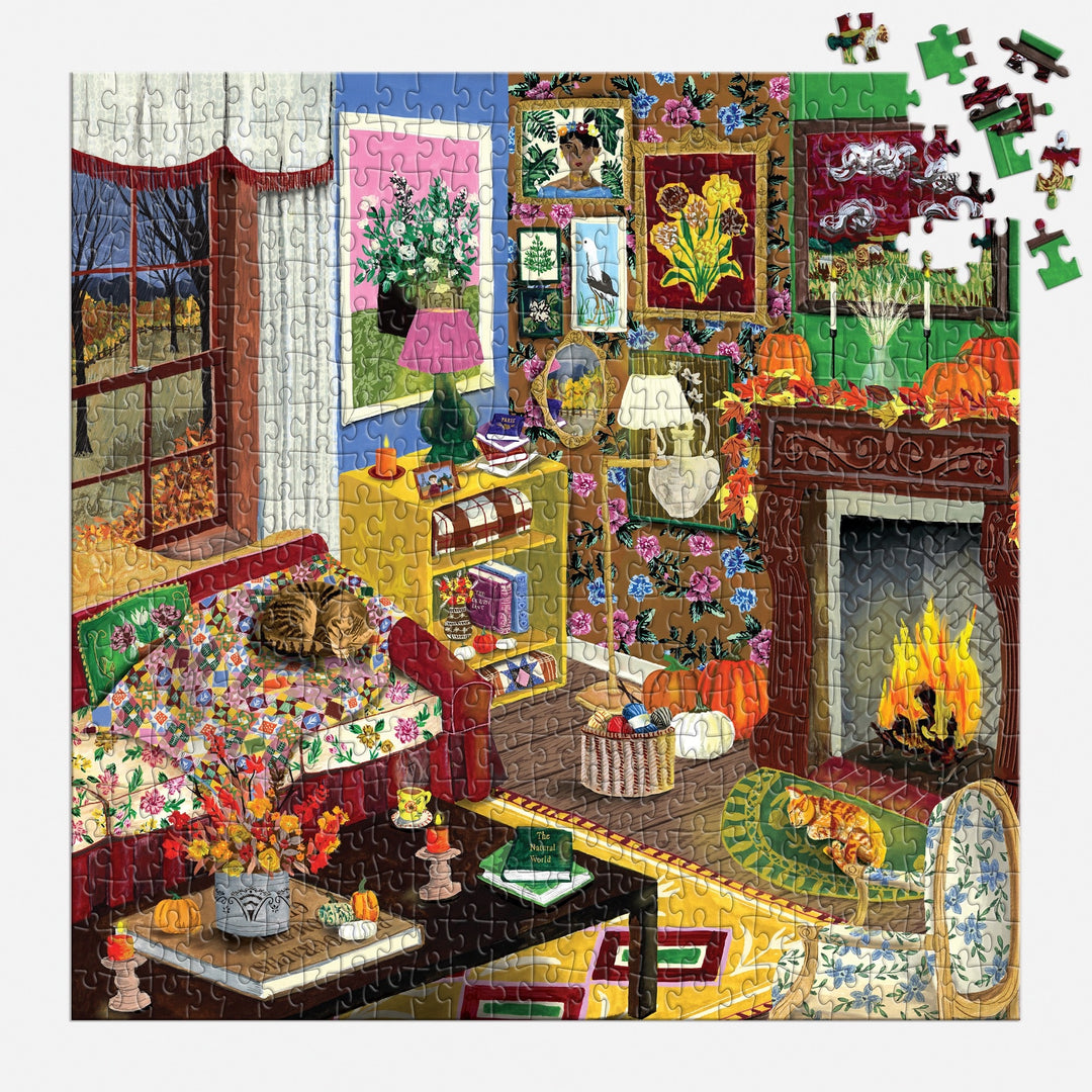 The "Fall is in the Air 500 Piece Puzzle" by Abbey Jacobs features a cozy room with a fireplace, patterned walls, plants, flowers, a cat on the bed, a pumpkin by the fire, and several pieces missing from the upper right corner.