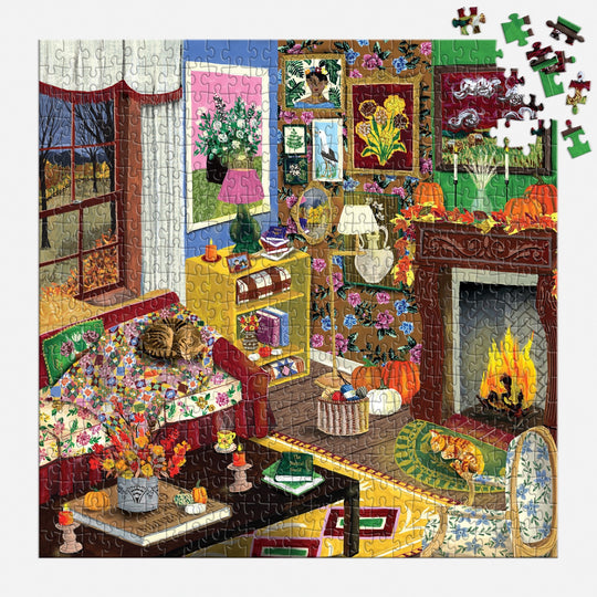 The "Fall is in the Air 500 Piece Puzzle" by Abbey Jacobs features a cozy room with a fireplace, patterned walls, plants, flowers, a cat on the bed, a pumpkin by the fire, and several pieces missing from the upper right corner.