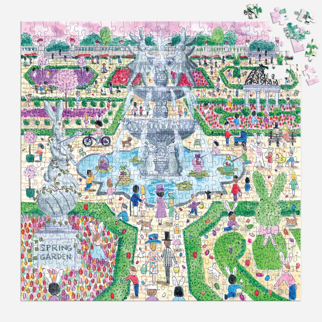 The Michael Storrings Spring Egg Hunt 500 Piece Puzzle features a vibrant garden scene with people, a central fountain, flower beds, statues, and a gazebo. Some puzzle pieces are missing in the upper right corner. Brand: Michael Storrings.