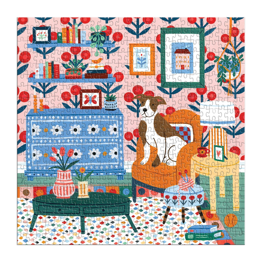 The Pattern & Petal 500 Piece Puzzle by Molly Egan features a colorful illustration of a cozy living room with vibrant wallpaper, bookshelves, a blue cabinet, orange armchair with a dog, green coffee table with flowers, and decor.