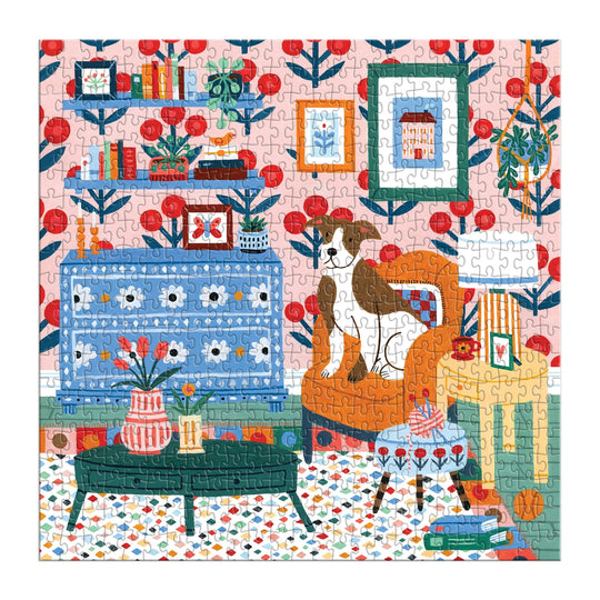 The Pattern & Petal 500 Piece Puzzle by Molly Egan features a colorful illustration of a cozy living room with vibrant wallpaper, bookshelves, a blue cabinet, orange armchair with a dog, green coffee table with flowers, and decor.