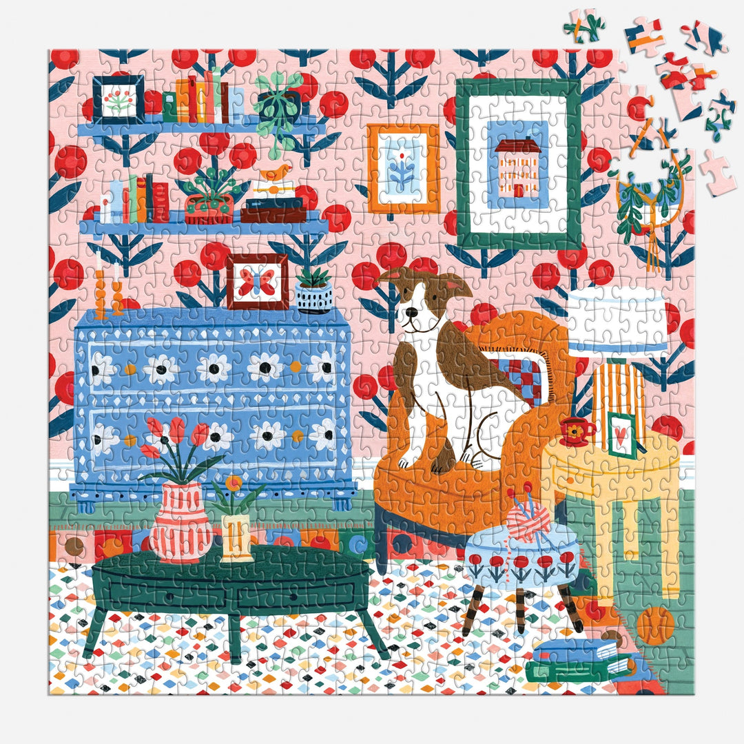 The Pattern & Petal 500 Piece Puzzle by Molly Egan features a cozy room with a dog on an orange chair, bookshelves, plants, colorful furniture on a patterned rug, and depicts the scene with a few pieces still missing.