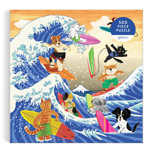 Yeji Yun’s The Great Surf 500 Piece Puzzle features cats and dogs riding vibrant surfboards on big ocean waves, a mountain in the background, and a “500-piece puzzle” label in the corner.