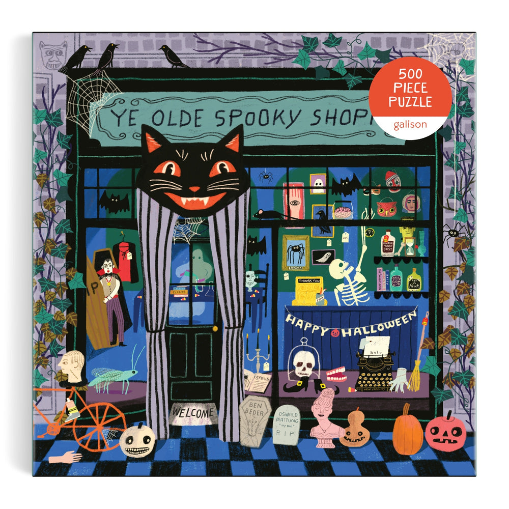 Ye Olde Spooky Shoppe 500 Piece Puzzle by Anne Bentley features a vibrant Halloween-themed storefront with a black cat sign, skeletons, pumpkins, potions, cobwebs, spooky decorations, and a Happy Halloween banner.